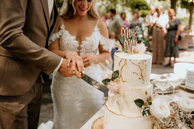 A bride and groom cut their elegant three tier wedding cake together at the outdoor reception.