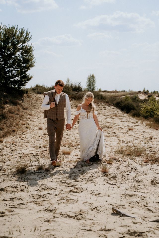 Bride and groom walking through sand dunes in light attire