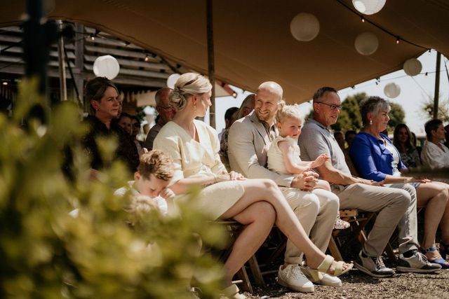 Wedding guests seated in rows under an outdoor tent watch the ceremony in a relaxed, joyful atmosphere.