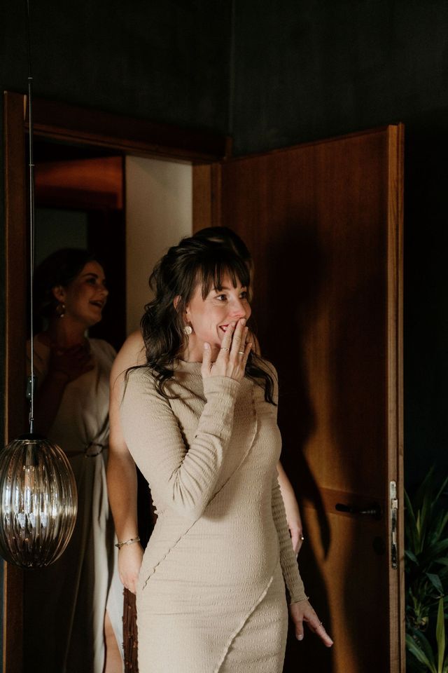A woman covers her mouth in an emotional reaction of joy, seeing the bride for the first time.