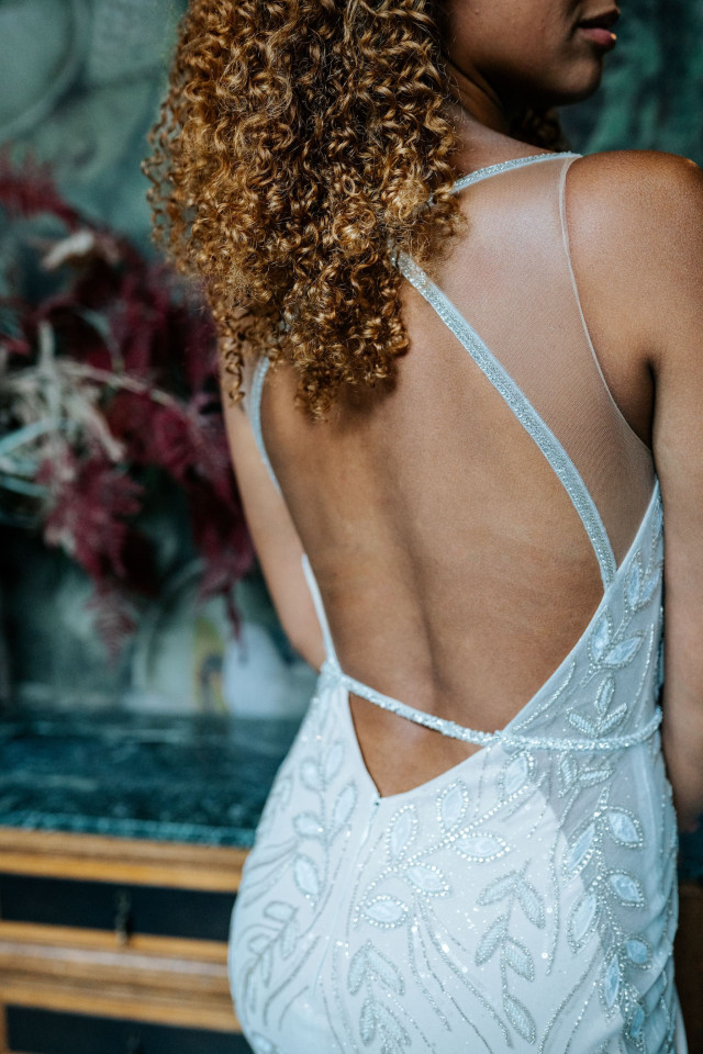 A bride with full, voluminous curly hair and an open-back beaded gown, seen from behind.