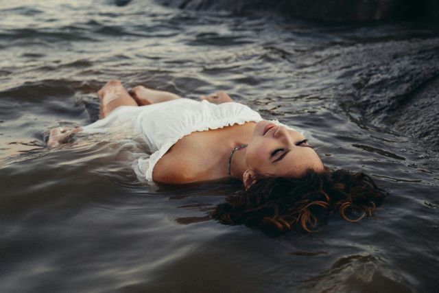 Frau liegt im Wasser und trägt ein weißes Kleid