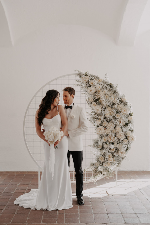 Brautpaar vor weißem Backdrop mit cremefarbenen Blumen