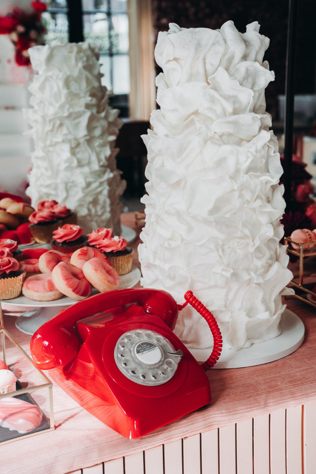Hochzeitstorte in Weiß mit Wasserfalleffekt steht neben einem knallroten Telefon mit Drehscheibe