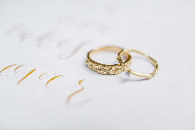 Twee gouden trouwringen op wit papier met kalligrafie