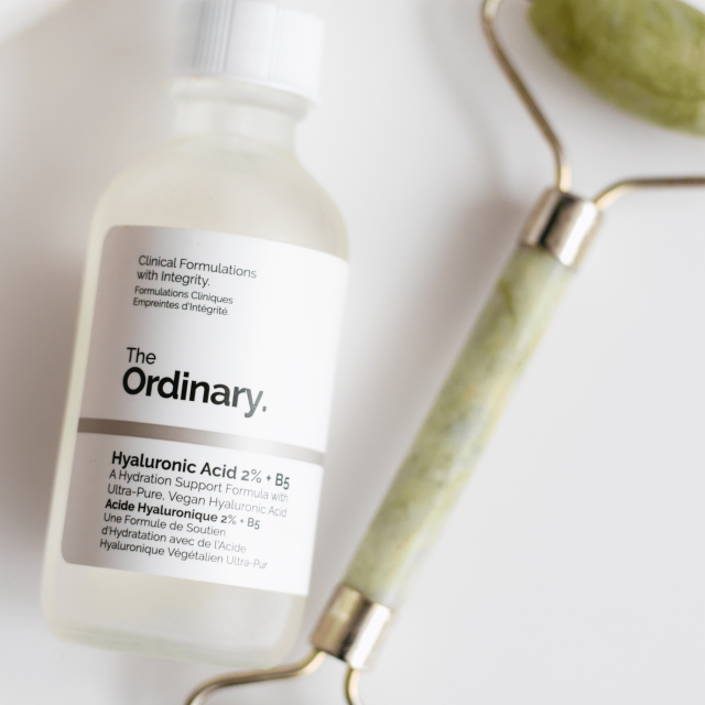 The Ordinary Flasche liegt auf weissem Untergrund neben einem gruenen Jaderoller