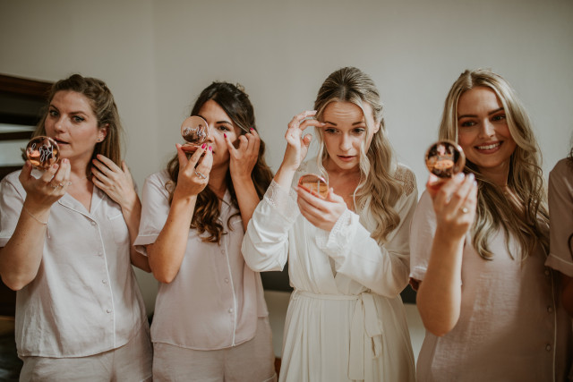 bruid met bruidsmeisjes die in make-up spiegeltjes kijken