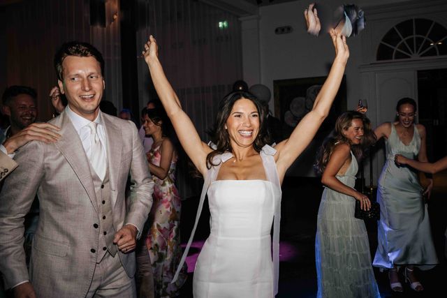 The couple joyfully enters the dance floor with their arms raised as guests cheer.