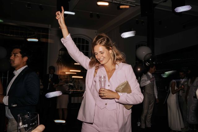 A guest in a pink suit dances with her arm raised and a drink in hand.