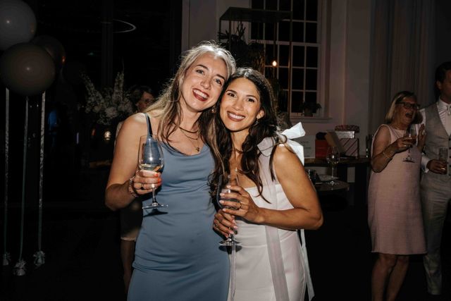 Two laughing guests pose with champagne glasses at a wedding reception.