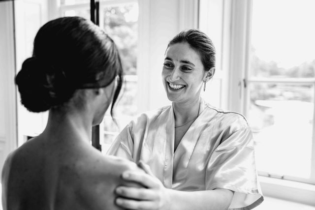 Friend in a satin robe with the bride during getting ready by a window