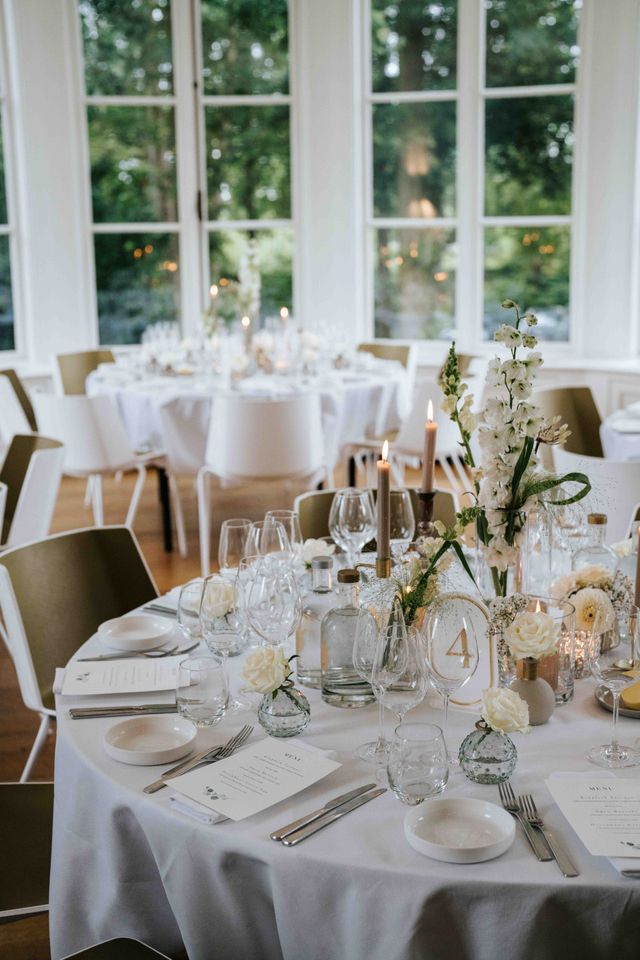 A festively set round table with white flowers, candles, and place settings.