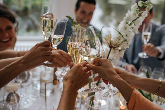 Gasten proosten met champagneglazen boven de gedekte tafel met witte orchideeën.