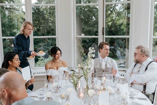 A server attends to the couple and their guests at the long reception table.
