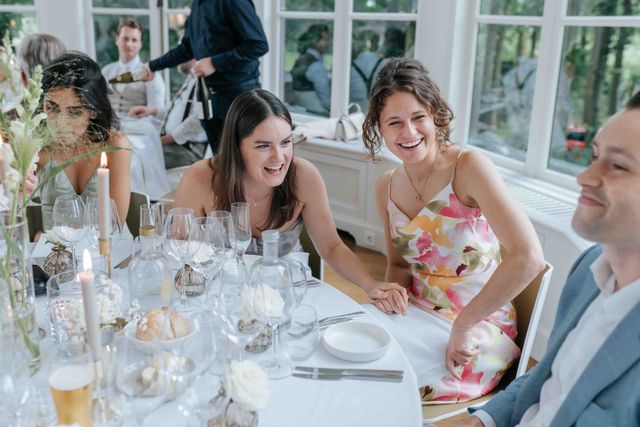 Guests sit laughing around an elegantly set outdoor dinner table at the reception.
