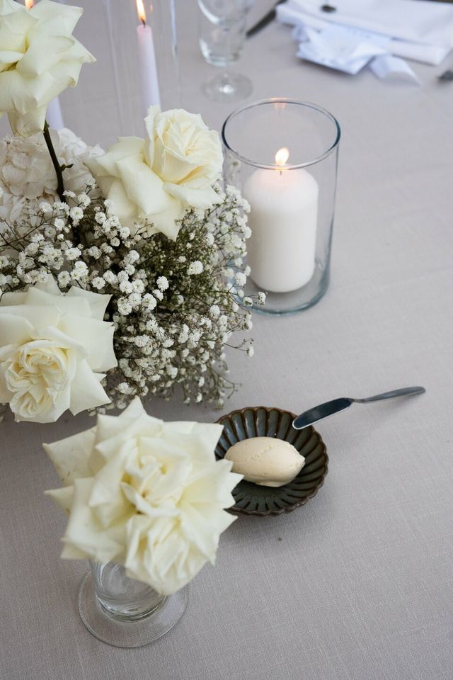 White roses and baby's breath with a lit candle and a handwritten name card.