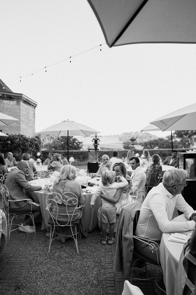 A black and white photo of guests dining at tables under parasols outdoors.