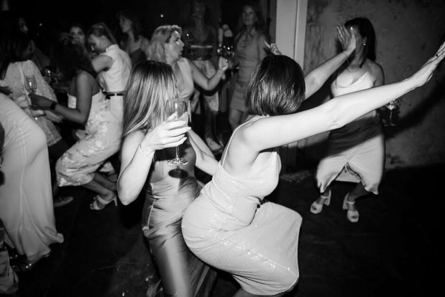A black and white photo of female guests dancing together with their arms raised.
