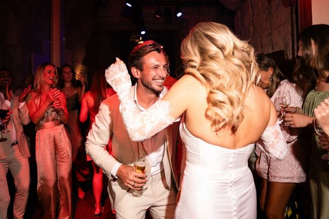 A bride and groom embrace closely on a busy, lively dance floor at the reception.