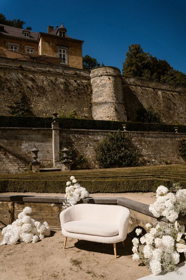 A white lounge sofa surrounded by lush white floral arrangements at a wedding.