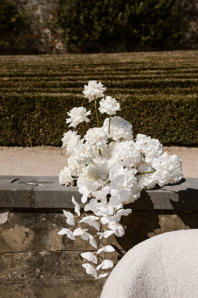 A white floral decoration of roses and hydrangeas on a stand at a wedding.