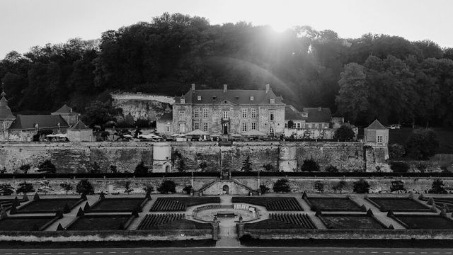 A black and white photo of a large castle on a hill with formal gardens in front.