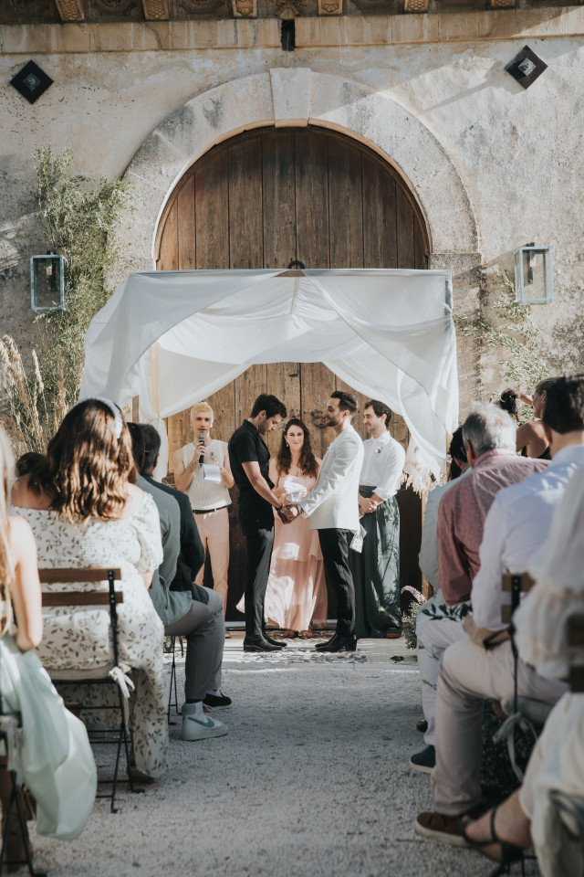 The couple stands before a wooden gate dressed with white drapery.