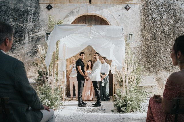 A ceremony set before an old stone gate dressed with white drapery.