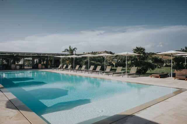 A large outdoor pool with loungers and parasols at a sunny Mediterranean venue.
