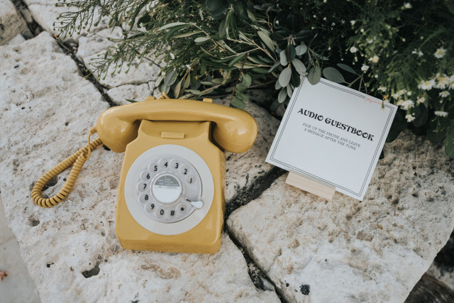 A yellow vintage rotary telephone beside a guestbook card and greenery.