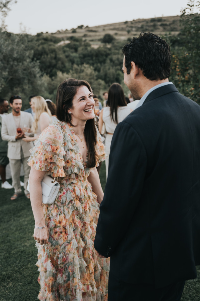 A laughing woman in a colorful floral dress with arms outstretched.