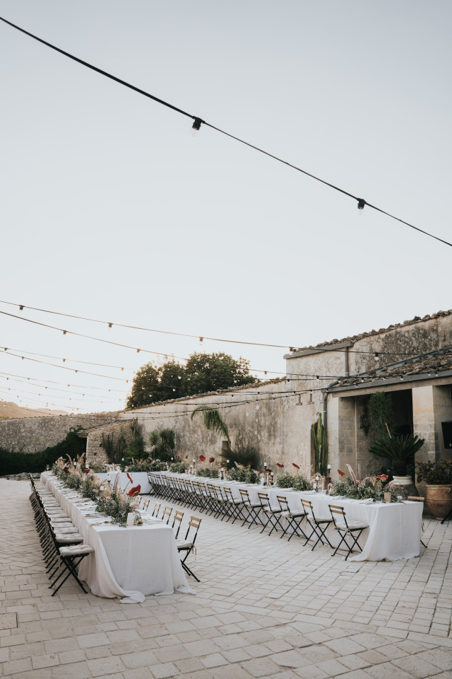 An overview of a spacious courtyard with long set tables and strings of lights.