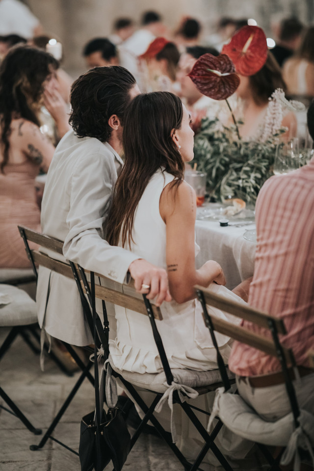 A couple sits close together at a long dinner table at the reception.