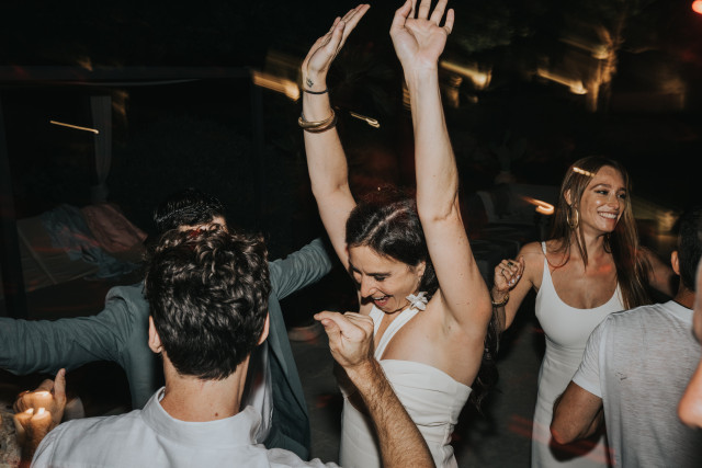 A bride and guests dance with their arms raised on the dance floor during the evening party.
