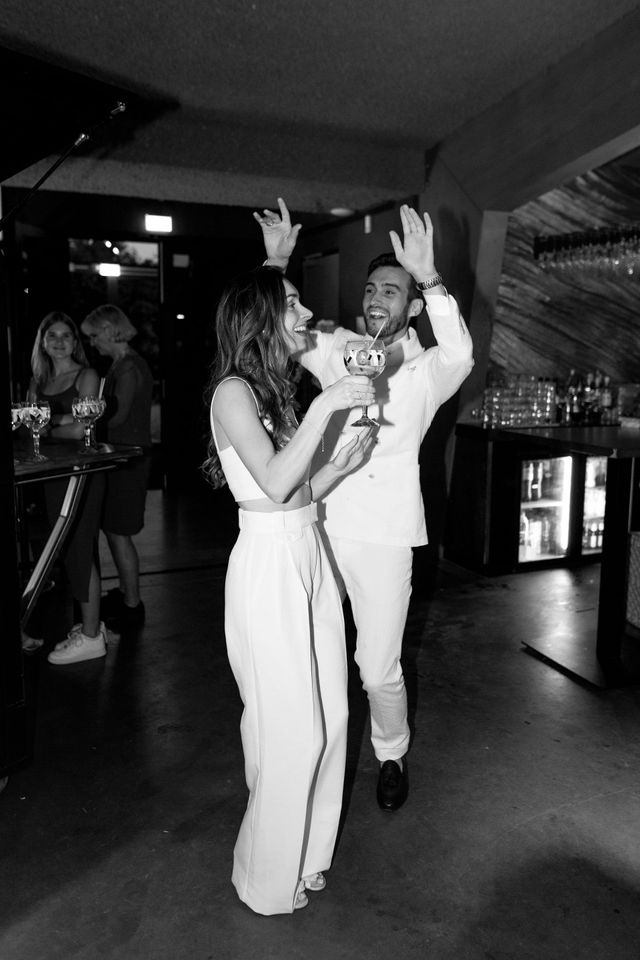 A bride and groom laugh and celebrate at the reception, the bride holding a trophy, captured in black and white.