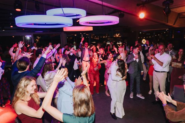 Guests fill the dance floor at a lively reception with colorful overhead lighting.