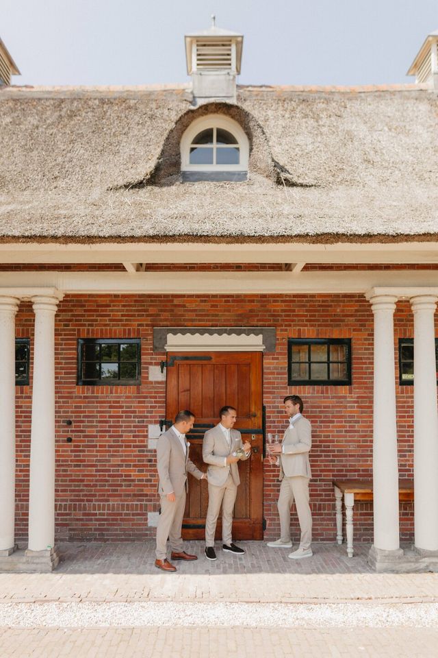 Groomsmen in light suits outside a rustic venue