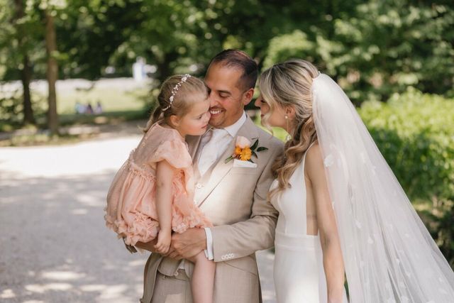 A bride and groom share a tender moment with a young flower girl in a pink dress before the ceremony.