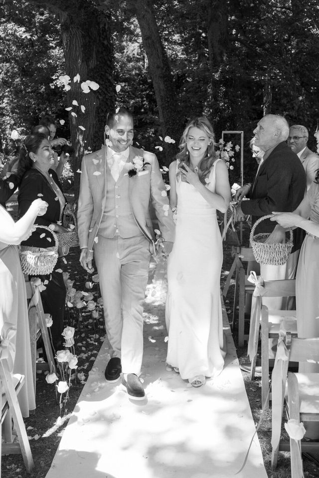 Black and white photo of the couple walking back down the aisle after the ceremony while guests toss flower petals.