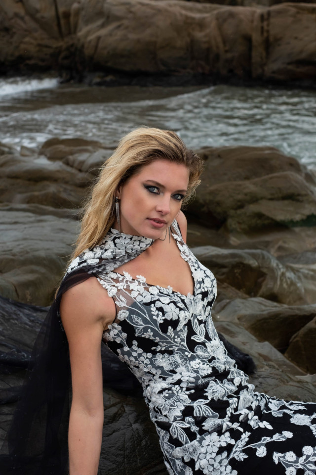 Braut in schwarz-weißem Brautkleid auf Steinen am Meer