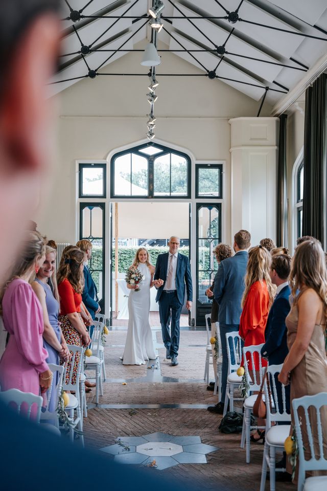 A bride walks down the aisle on the arm of a man as guests look on.