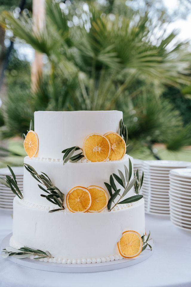 A three-tier white wedding cake decorated with dried orange slices and olive branches.