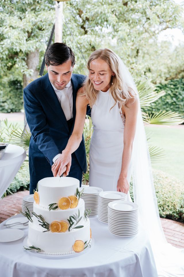 The couple laughs together as they cut into their white wedding cake.