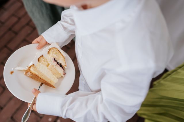 A guest holds a small plate with a slice of wedding cake at the reception.