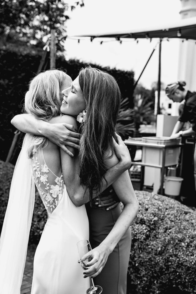A black and white photo of the bride in a veil greeting a guest with a drink.