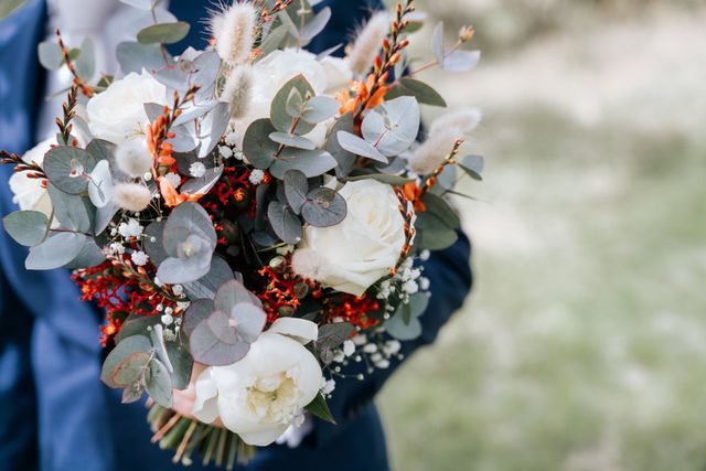 A bridal bouquet of white roses, eucalyptus and warm orange berries.