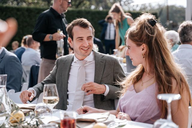 A man in a blazer and a woman in a lilac dress laugh together at the celebration.