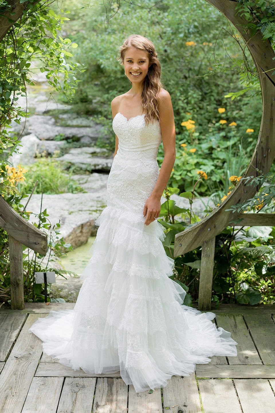 een prachtige bruid in een strapless bruidsjurk die op een houten brug staat