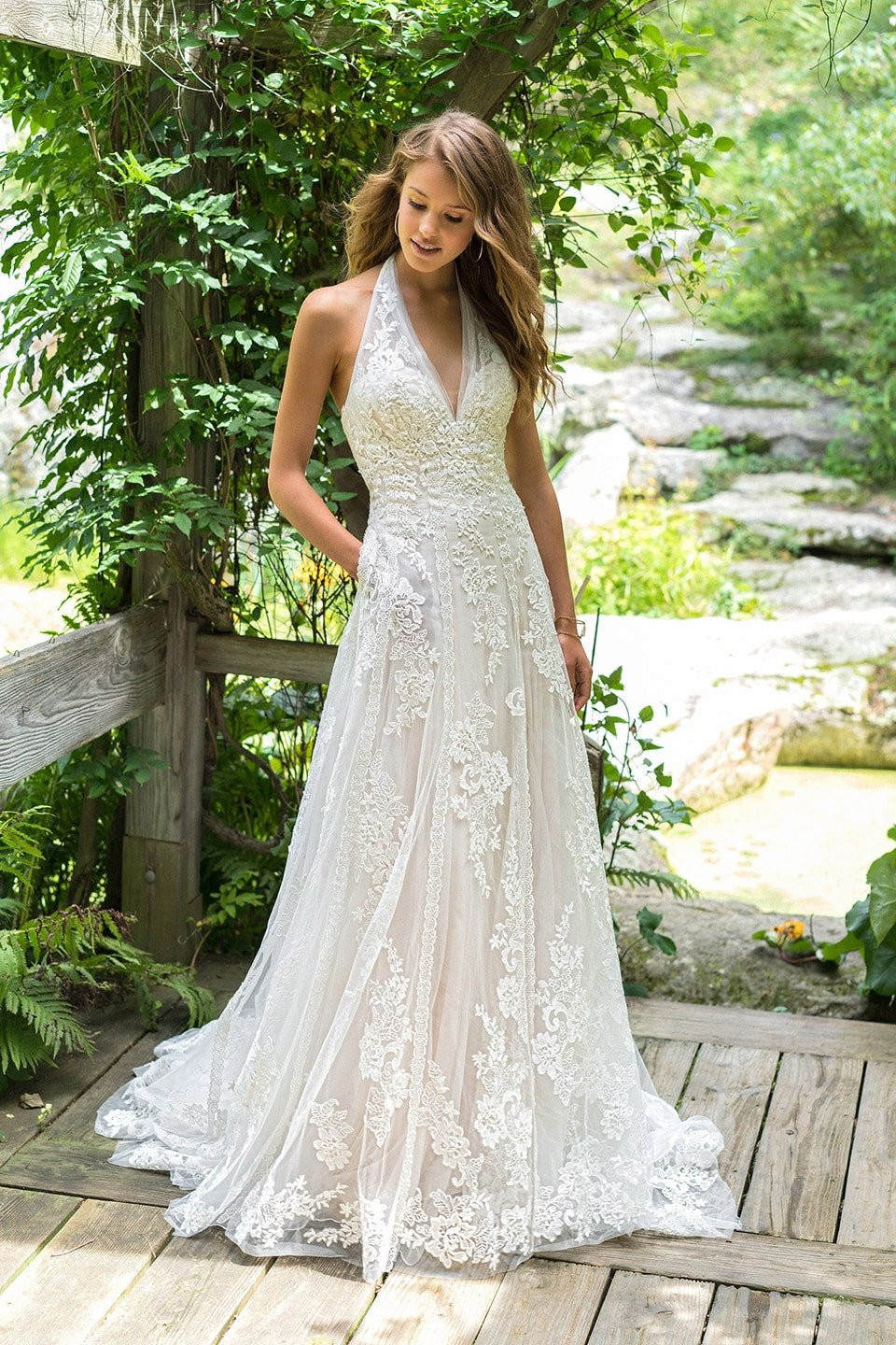 een mooie vrouw in een trouwjurk die op een houten brug staat