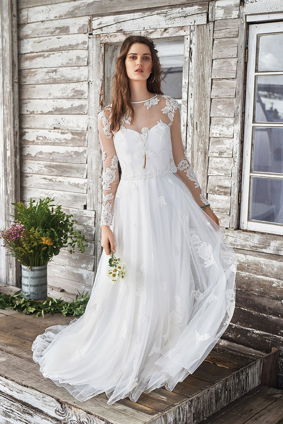 de bruid draagt een trouwjurk met lange mouwen en een doorschijnend lijfje